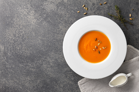 Pumpkin soup with seeds in a big white plate on gray stone backgroundの写真素材