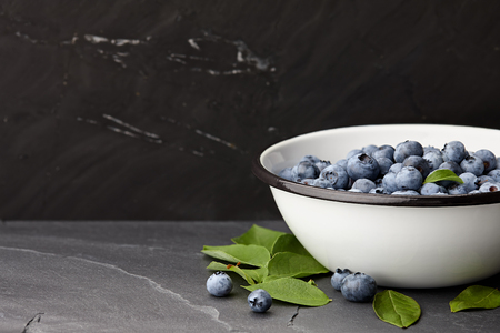 Fresh ripe blueberries with leaves bowl on black stone countertopの写真素材