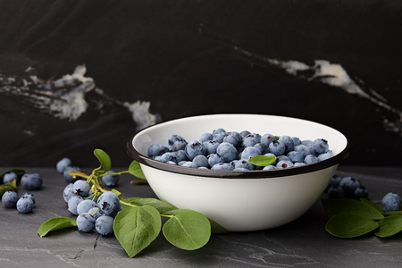 Fresh ripe blueberries with leaves bowl on black stone countertopの写真素材