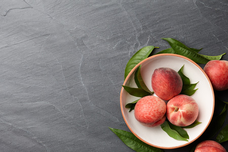 Fresh peaches fruits with leaves on textured stone background, top viewの写真素材