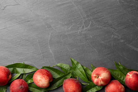 Fresh peaches fruits with leaves on textured stone background, top viewの写真素材