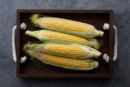 Sweet corns in wooden tray on a stone textured background, top viewの写真素材