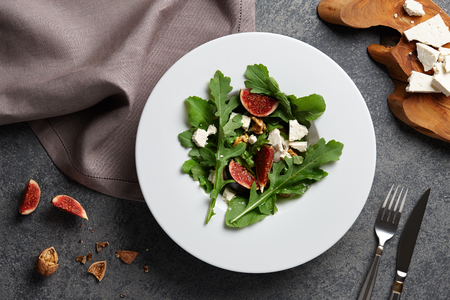 Seasonal salad with figs, arugula, walnuts and feta cheese on textured stone backgroundの写真素材