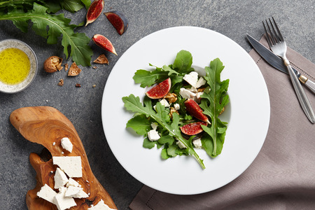 Seasonal salad with figs, arugula, walnuts and feta cheese on textured stone backgroundの写真素材