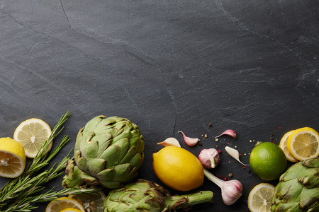 Fresh artichokes with lemons and garlic on dark stone background, top viewの写真素材