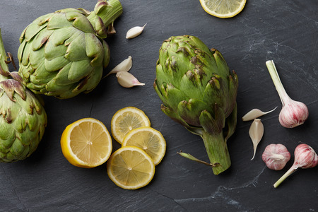 Fresh artichokes with lemons and garlic on dark stone background, top viewの写真素材