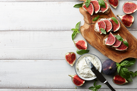 Fresh figs, basil leaves and philadelphia cream cheese bruschetta on white wooden table, top viewの写真素材