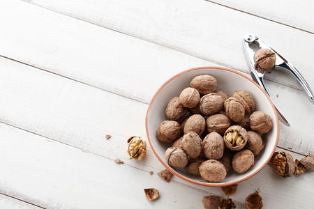 Fresh walnuts bowl, nutshell and nutcracker on white wooden background, space for textingの写真素材