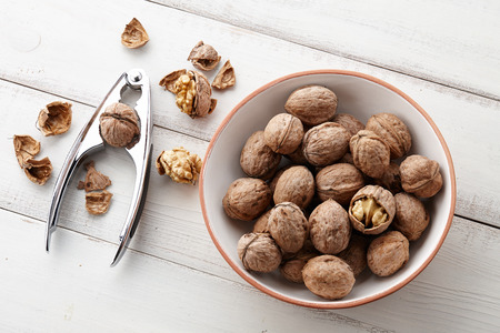 Fresh walnuts bowl, nutshell and nutcracker on white wooden backgroundの写真素材