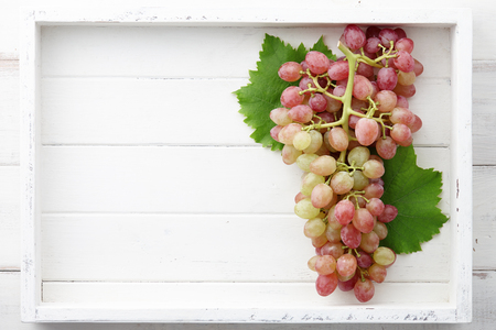 Red grapes bunch with leaves in white wooden tray, space for textingの写真素材