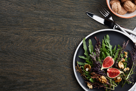 Seasonal salad with figs, walnuts and fresh greens on wooden background, top viewの写真素材