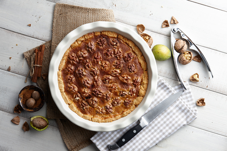 Traditional walnut pie with nuts and nutcracker on white wooden planks, top viewの写真素材