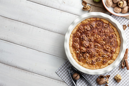 Traditional walnut pie with nuts and nutcracker on white wooden planks, top viewの写真素材
