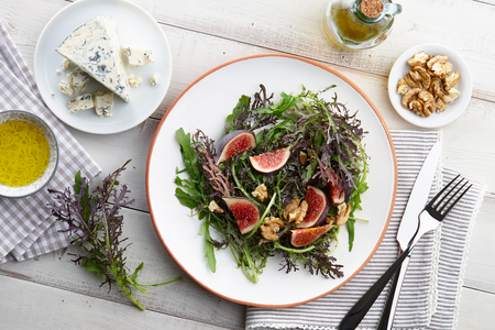 Salad with figs, blue cheese, arugula, mizuna and walnuts on white wooden background, top viewの写真素材