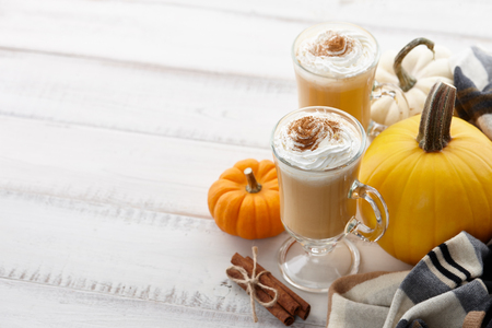 Fall pumpkin spice latte with whipped cream and cinnamon, ornamental pumpkins and warm woolen scarf on white wooden background, copyspaceの写真素材