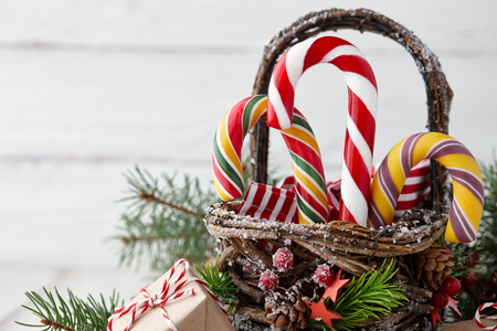Christmas wicker basket with striped candy canes and gifts on white wooden table, festive decorationの写真素材