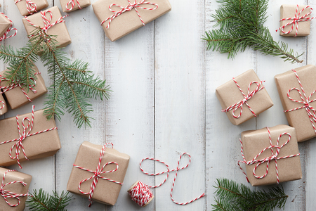 Christmas presents and gift boxes wrapped in kraft paper and fir tree decorations on white wooden background, copy spaceの写真素材