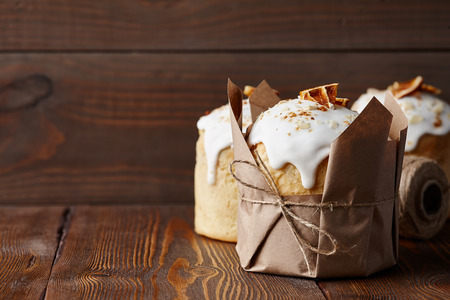 Easter cakes with candied fruits and almond crumbs wrapped in kraft paper on brown wooden tableの写真素材