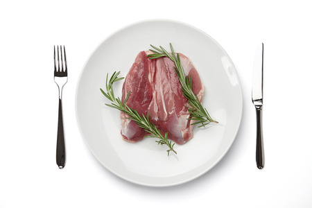 Raw duck fillet with rosemary in big round plate and cutlery isolated on white background, top viewの写真素材