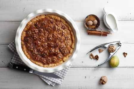 Traditional walnut pie with nuts and nutcracker on white wooden planks, top viewの写真素材
