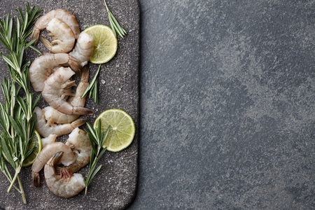 Cooking fresh raw tiger prawns with rosemary, lemon, lime, garlic and spices on stone countertop, top viewの写真素材