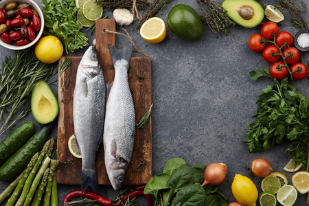 Fresh raw seabass and ingredients for cooking: rosemary, thyme, lime, lemon, greens and vegetables. Top view, copyspaceの写真素材