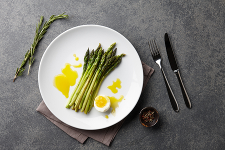 Baked asparagus with boiled egg in big white plate on stone background, top viewの写真素材