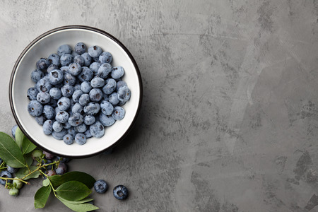 Fresh ripe blueberries with leaves in bowl on gray stone background, top viewの写真素材