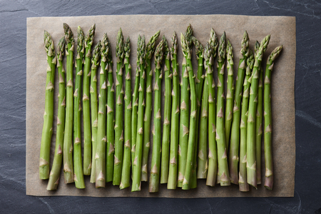 Green asparagus on a baking paper on dark stone background, top viewの写真素材