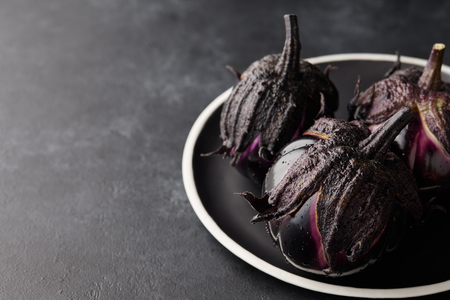 Fresh Italian type eggplants or aubergines with water drops in black plate on dark stone backgroundの写真素材