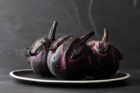 Fresh Italian type eggplants or aubergines with water drops in black plate on dark stone backgroundの写真素材