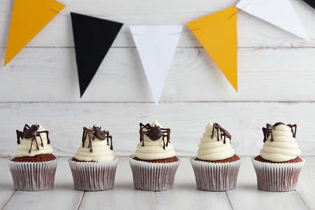 Halloween cupcakes with chocolate spiders in a row on wooden planks with festive orange, black and white garlandの写真素材