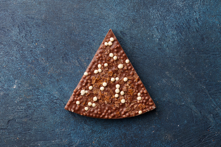 Triangle shaped piece of milk handmade chocolate with rice balls and flakes on blue background, top viewの写真素材