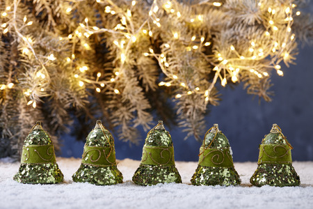 Shiny green Christmas bells on snowy table on fir tree lights backgroundの写真素材