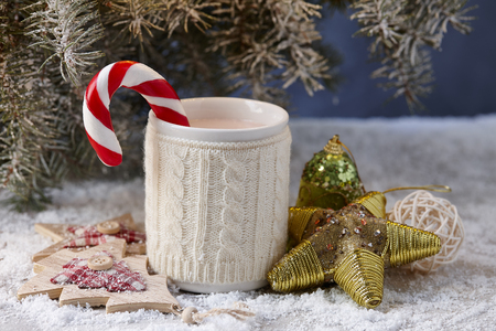 Knitted winter cup with hot chocolate and candy cane on snowy table under christmas treeの写真素材