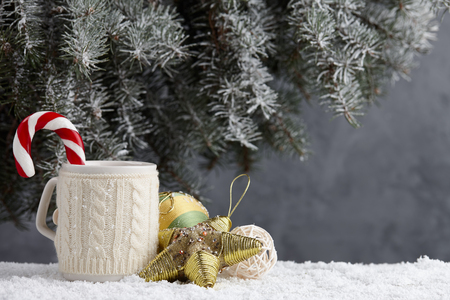 Knitted winter cup with hot chocolate and candy cane on snowy table under christmas treeの写真素材