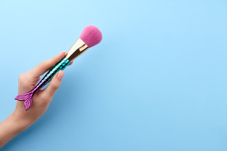 Womans hand holding make up brush on blue background, top viewの写真素材