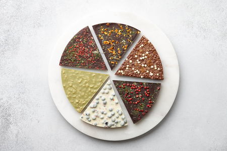 Round chocolate pizza pieces with diverse kinds of chocolate on stone tray on textured background, top viewの写真素材