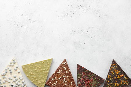 Triangle or pizza slice shaped chocolate pieces with diverse kinds of toppings on white textured background, copy spaceの写真素材