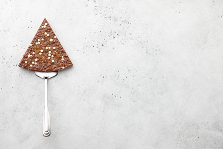 Pizza slice or triangle shaped chocolate piece on metal spatula on stone backgroundの写真素材