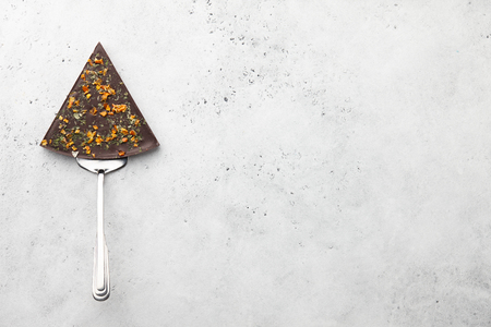 Pizza slice or triangle shaped chocolate piece on metal spatula on stone backgroundの写真素材