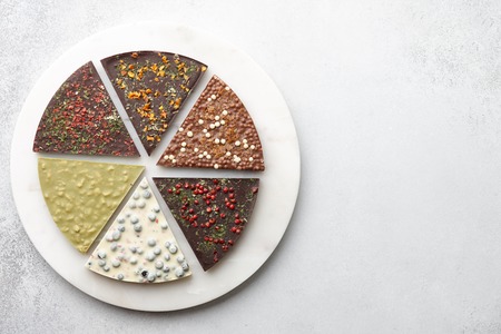 Round chocolate pizza pieces with diverse kinds of chocolate on stone tray on textured background, top viewの写真素材