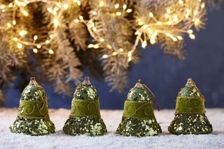 Shiny green Christmas bells on snowy table on fir tree lights backgroundの写真素材