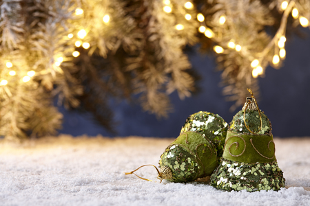 Shiny green Christmas bells on snowy table on fir tree lights backgroundの写真素材