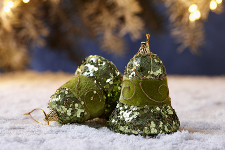 Shiny green Christmas bells on snowy table on fir tree lights backgroundの写真素材