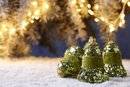 Shiny green Christmas bells on snowy table on fir tree lights backgroundの写真素材