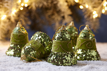 Shiny green Christmas bells on snowy table on fir tree lights backgroundの写真素材