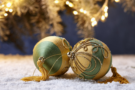 Green and golden colored Christmas balls on snowy table on tree lights backgroundの写真素材