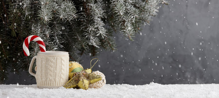 Knitted winter cup with hot chocolate and candy cane, christmas toys in snow under christmas tree. Holiday concept.の写真素材