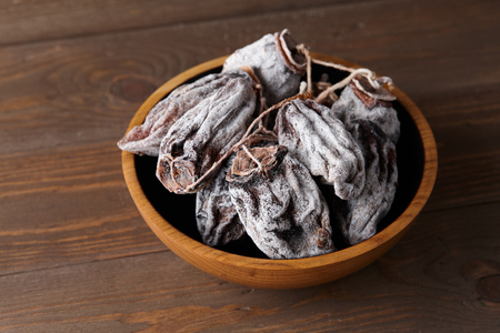 Dried persimmon in wooden bowl on planks background, close up viewの写真素材